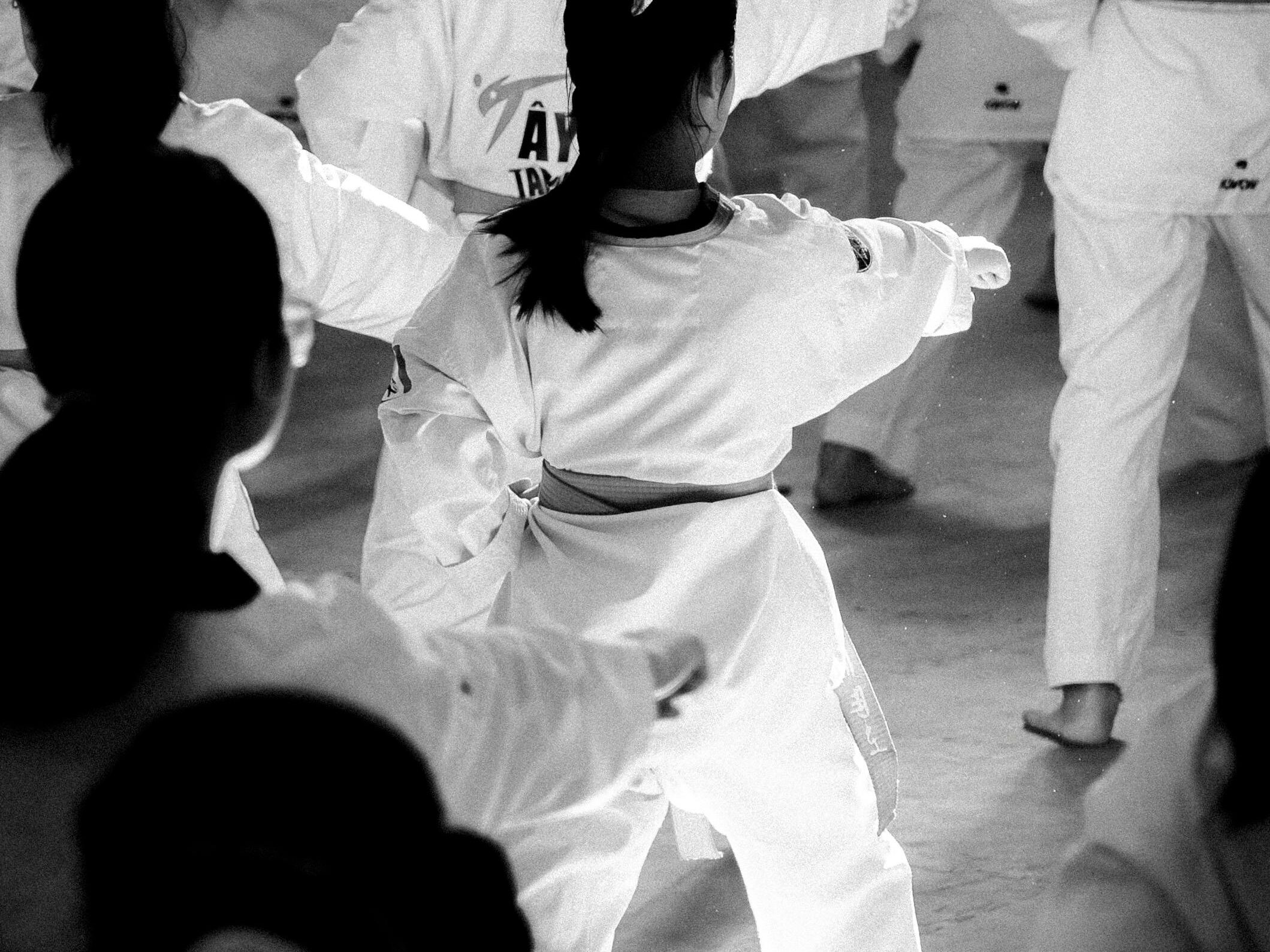 A group of karate students practicing in a well-lit training hall, captured in black and white.